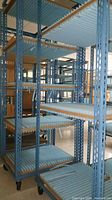Side view of tall blue metal shelving racks with wooden and conveyor roller shelves and caster wheels