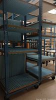 View of several tall blue metal shelving racks with multiple ribbed shelves on casters in large room.