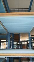 View looking through the shelves of one of the metal racks showing wooden plank shelves and blue metal frame structure