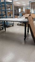 Full view of the rectangular plastic table on wheels inside a room with shelving and other storage equipment.