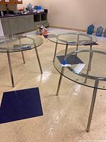 Three round glass top metal tables viewed from above in a room with tiled floor and some water dispensers in the background.