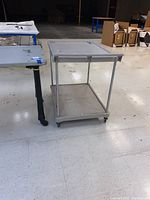 Photo shows metal rolling cart with two flat surfaces and wheels.