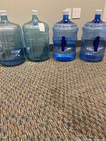 Five large water bottles on a carpeted floor, showing overall lot contents.