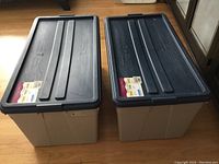 Photo showing two large storage containers with blue lids and beige bases, labeled with brand and capacity info.