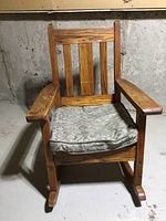 Front view of antique wooden Mission style rocking chair with removable patterned seat cushion on it.