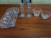 Pair of crystal taper candlestick holders, Cross and Olive condiment dish, and cream and sugar set on wood surface