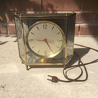 Front view of the electric clock showing the round face, glass case with brass frame, and power cord on a concrete surface.