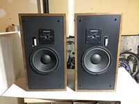 Front view of two Genesis speakers showing wooden cabinets, black fronts, large woofers, adjustment knobs and sliders, no grills.