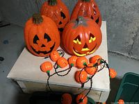 Four large orange plastic jack-o'-lantern pumpkins with glitter detail and pumpkin-shaped string lights on a wooden table