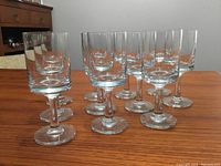 Eleven heavy glass wine glasses arranged on a wooden surface, showing the front view of the glasses clustered together.