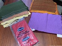 Image showing assorted folded placemats in colors like green, yellow, purple, brown, orange, and one new packaged red tablecloth.