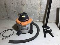 Ridgid shop vacuum with hose and three different black plastic cleaning attachments on the concrete floor.