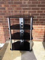 Front view of the TV or stereo stand showing four black glass shelves and chrome cylindrical legs.