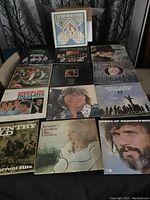 Photo of first 15 vinyl record albums with various country music artists with visible album covers and titles, placed in two rows on a sofa.