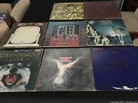 8 rock vinyl albums laid out on a black table showing front covers with some visible wear and damage to edges and corners