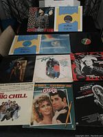 Image showing 11 vinyl records including soundtracks and singles arranged on a table with album covers and some vinyl sleeves visible.