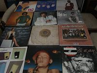 Photo showing 12 vinyl record covers laid out in a grid on a table, featuring 'We Are The World' and other 1980s music albums.