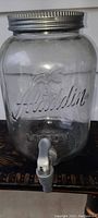 Front view of glass dispenser showing embossed Aladdin logo and front pour spout.