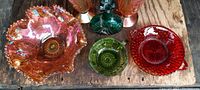 View of the lot showing large orange carnival glass bowl, green decorative bottle, red dish, and smaller bowls.