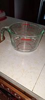 Side view of the clear Pyrex measuring bowl on countertop, showing red measurement markings and handle