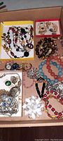 Overview of the assortment of costume jewelry showing beaded necklaces in red, black, cream colors, colored bracelets in coral and blue, multiple pins including heart shapes, and small watches.