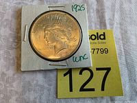 Front side of the 1925 Peace silver dollar in an uncirculated condition holder with '1925 unc' written.