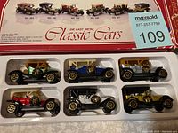 Photo showing six die cast metal classic cars in original plastic tray within box. Cars vary in color with detailed vintage designs.