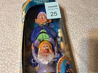 Front view of the Dopey and Sneezy stackable dolls in original box packaging showing characters and branding.