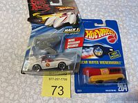 Photo of two Hot Wheels cars in packaging: Speed Racer Mach 5 with saw blades and Oscar Mayer Wienermobile
