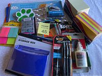 Photo of assorted office and school supplies including planner, sticky notes, pens, glue, stapler, and storage box.