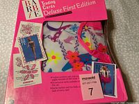 Bright pink sealed box of Barbie Trading Cards Deluxe First Edition featuring Barbie images and fashion designs on packaging.