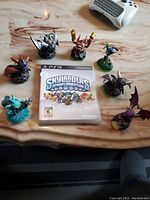 Top view showing all 7 Skylanders figures arranged around the PS3 Skylanders Spyro's Adventure game case on a wood-grain table with a game controller in the background.