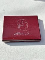 Closed red box with white profile image and signature of George Washington on lid