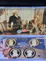 Top view of the 2008 United States Mint Presidential $1 Coin Proof Set showing four proof coins in individual slots inside a clear plastic case, held against the decorative presentation box backdrop.