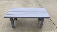 Photo showing top view of rectangular grey outdoor table with slatted metal top and four sturdy legs on concrete surface.
