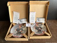 Two collector plates from the 'Lucy I Just Like Candy' design in open cardboard boxes with vintage store front and Lucy artwork visible.