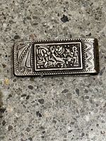 Front side of the silver money clip showing detailed engraved figure and decorative border.