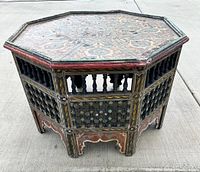 Front angled view of the vintage octagonal Moroccan style wooden table showing intricate spindles and painted surface with signs of age.