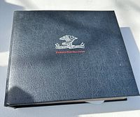 Photo of binder showing the black textured cover with an eagle emblem and red text reading 'Philatelic First Day Covers'.