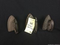 Three antique sad irons each with distinct handle styles and visibly aged metal bases, photographed together on black background to show condition and differences.