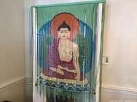 Green bead hanging screen depicting seated Buddha with orange and blue circular backdrop, hanging from a wooden rod with loops.
