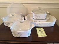 Corning Ware Shadow Iris casseroles arranged with glass lids and plastic storage lids visible, showing floral pattern on white ceramic body.