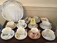 Front view of six floral teacups and saucers, two decorative china shoes, and large Mikasa platter behind.