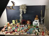 Wide view of the full collection showing assorted Christmas ornaments, candle holders, a plush reindeer, acrylic deer figures, and tinsel garlands arranged in front of a black background.