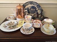 Overview of teacups, saucers, teapot with copper cover, and large decorative plate