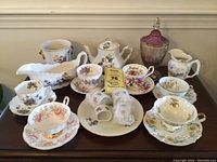 Overall collection of vintage porcelain tea set with multiple floral teacups, teapot, and serving pieces on wooden table