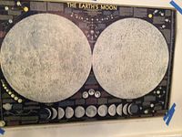 Photo of The Earth's Moon poster showing detailed maps of the lunar surface with phases and informational text, paper poster taped to wall