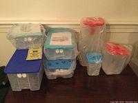 Seven new Tupperware containers with colorful lids in blue, teal, and red, all wrapped in plastic, displayed on a table.