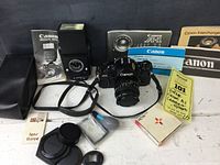 Overview of Canon A-1 camera with 50mm lens, flash unit, filters, manuals and accessories arranged on a white surface.