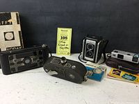 Lot containing Kodak Jiffy 5X-16 folding camera in original box, Keystone 8mm Model K-8 movie camera, Kodak Duaflex III camera with instructions, and Kodak Pocket Instamatic 10 with carrying case and instructions displayed on table